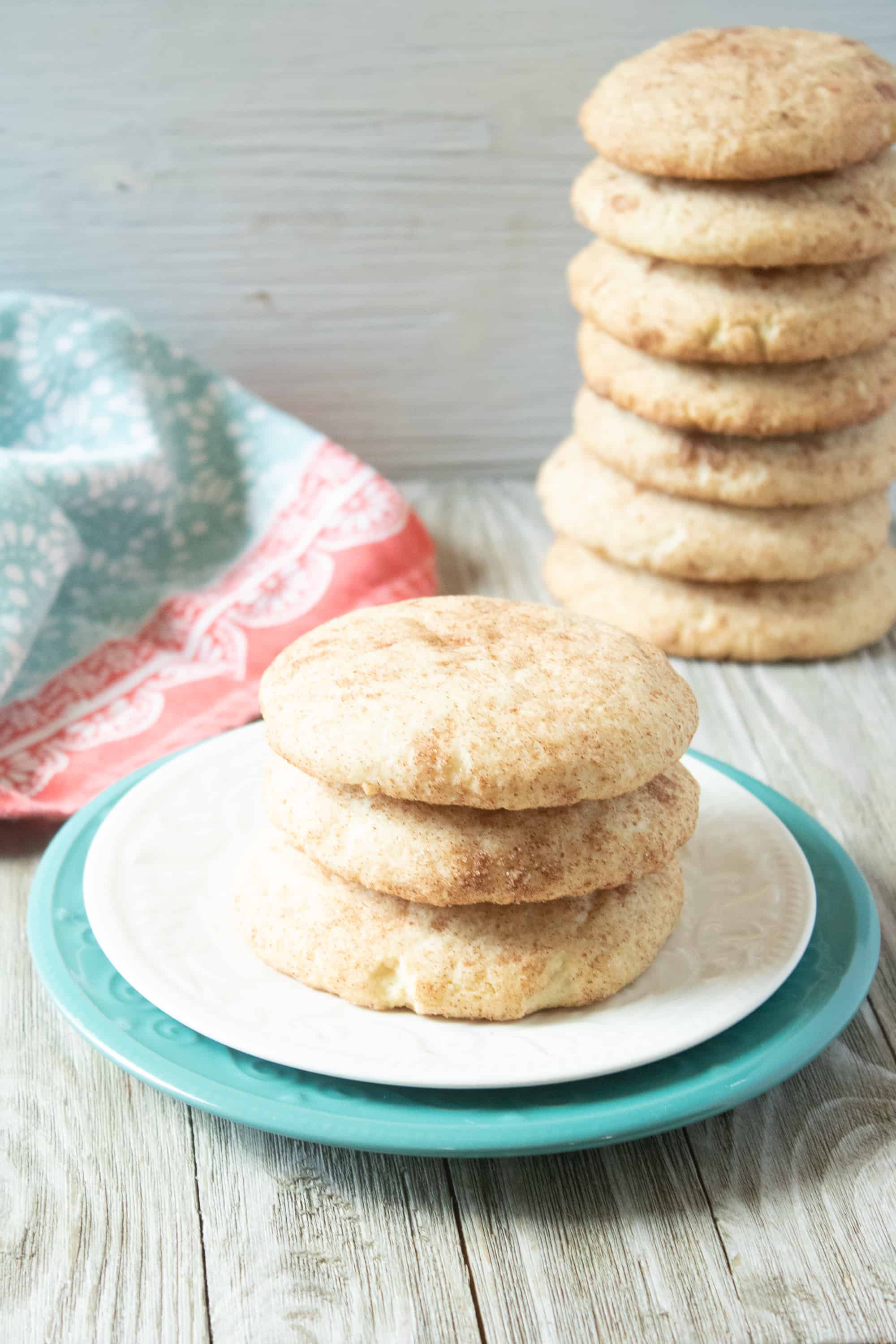 stack of snickerdoodles on white and teal plates, with a huge stack of cookies in the background