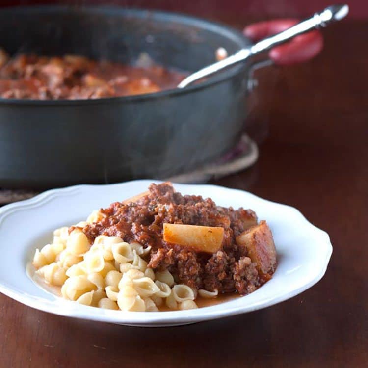 goulash in white bowl with pan of goulash in the background