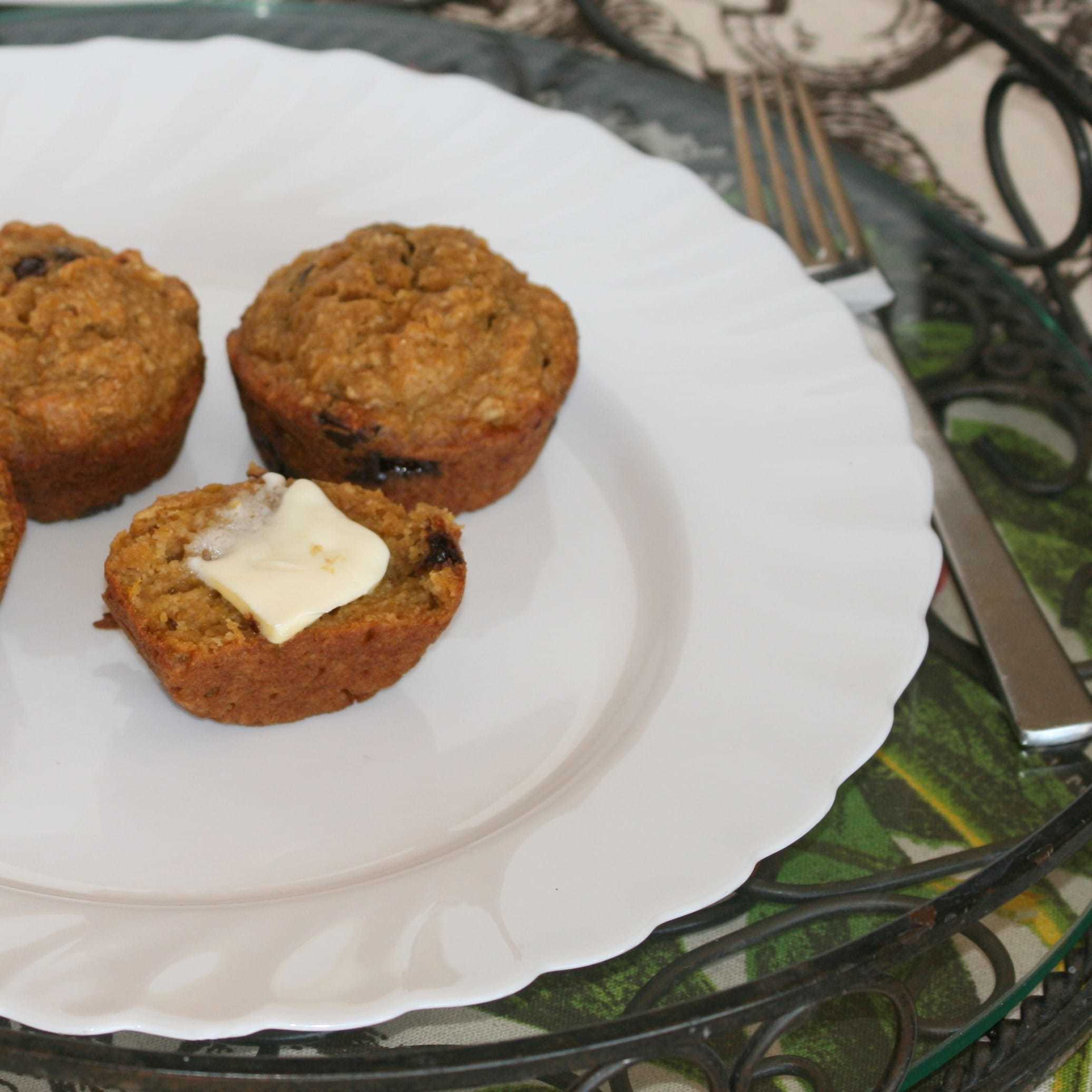 Pumpkin chocolate chip muffins on a white plate, one split open with a pat of butter