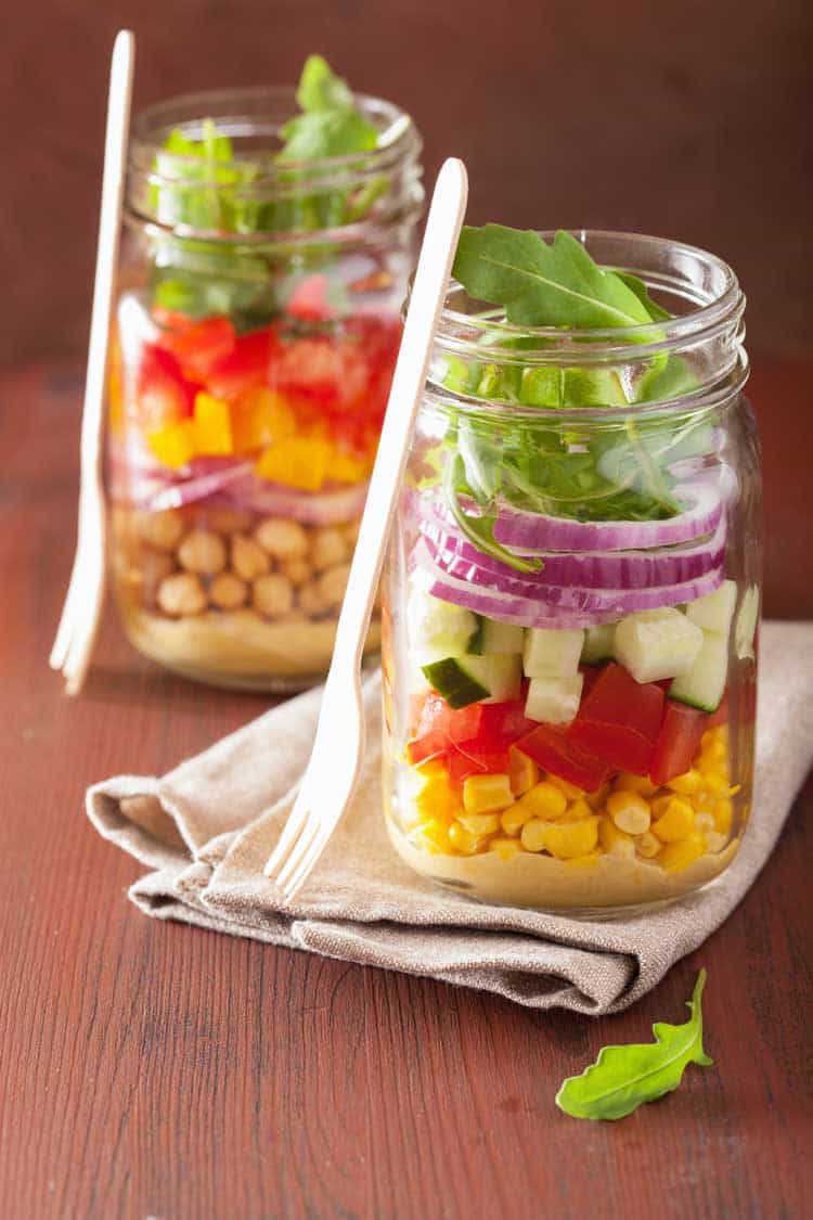 mason jar salad in two mason jars filled with colorful vegetables in layers next to a fork