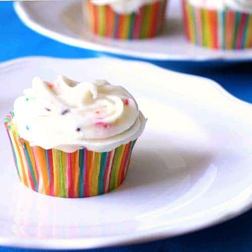 closeup of a lemon cupcake with cream cheese frosting with sprinkles sitting on a white plate