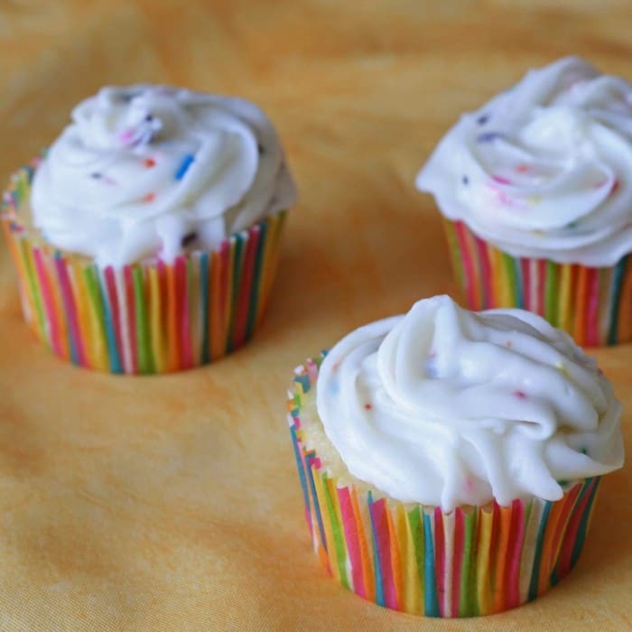 three lemon cupcakes on a brown countertop each with cream cheese frosting on top