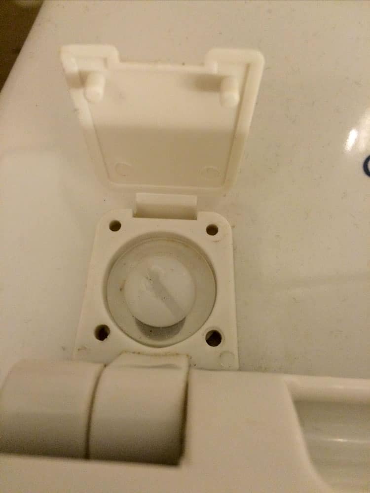 Toilet seat hinge with its plastic cover flipped open to show the bolt underneath