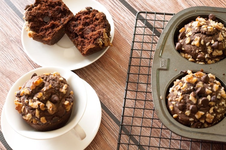 Overhead view of chocolate banana nut muffins, one split open, beside a jumbo muffin pan on a cooling rack