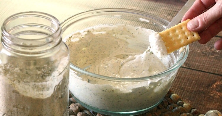 glass jar with dry ranch dip next to a bowl with hand dipping into ranch dip