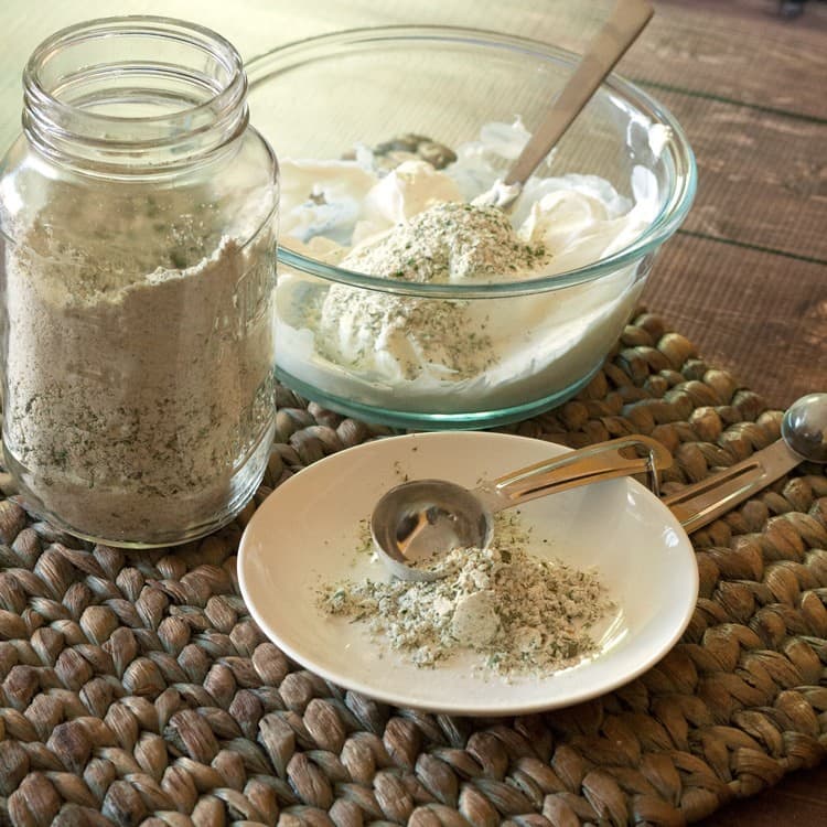 white plate containing measuring spoon and ranch dip in front of a jar with ranch dip and bowl with ingredients