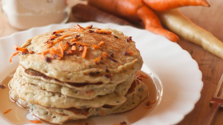 carrot pancakes on a white plate with carrots on top and syrup drizzled on top