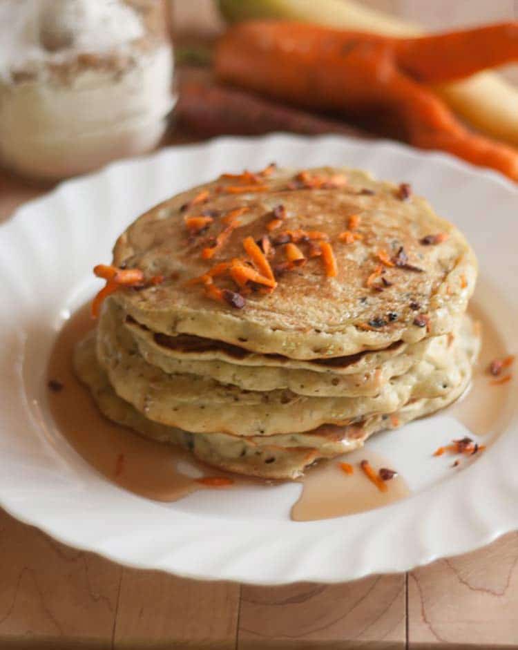 closeup of sweet carrot pancakes with diced carrots on top and syrup drizzled around