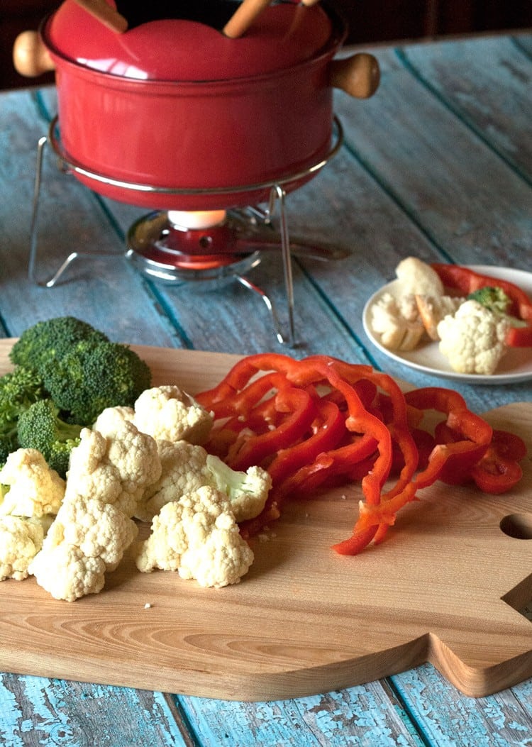 cheddar cheese fondue in a red pot behind a cutting board of raw vegetables