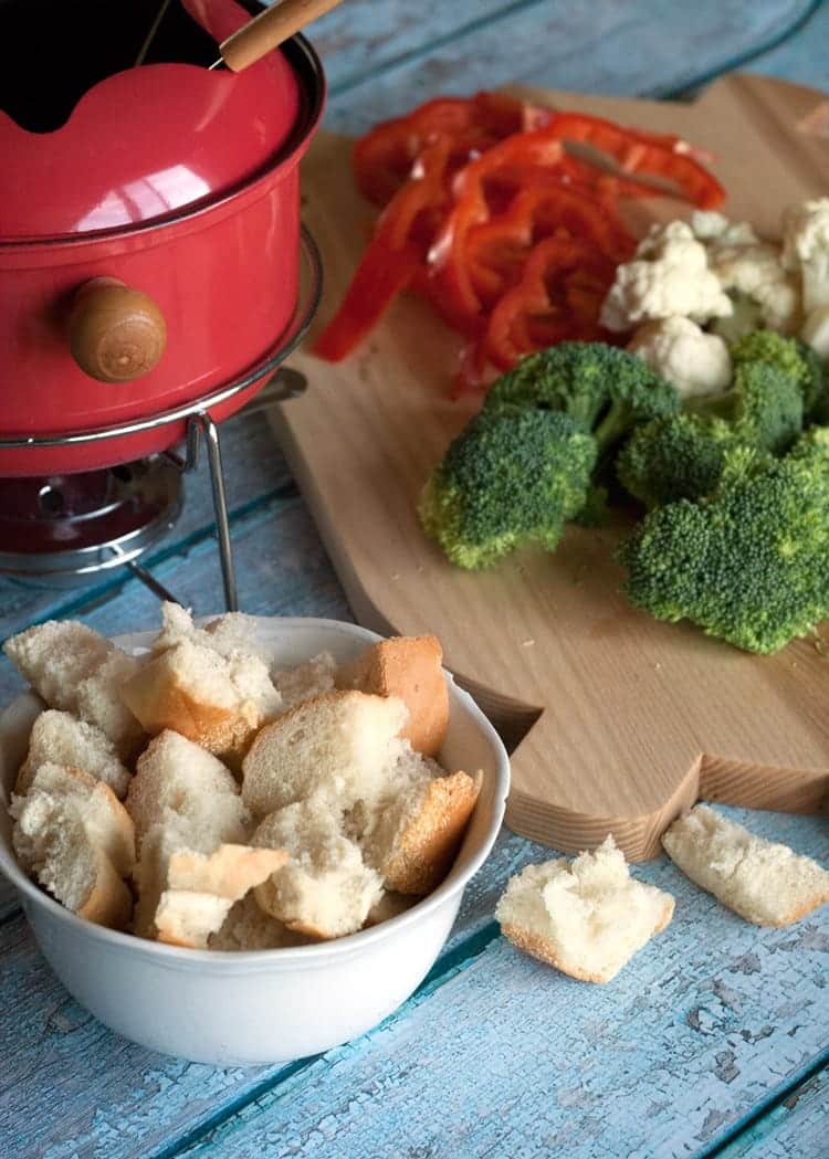 closeup of white bowl containing bread pieces in front of a fondue pot with cheddar cheese fondue