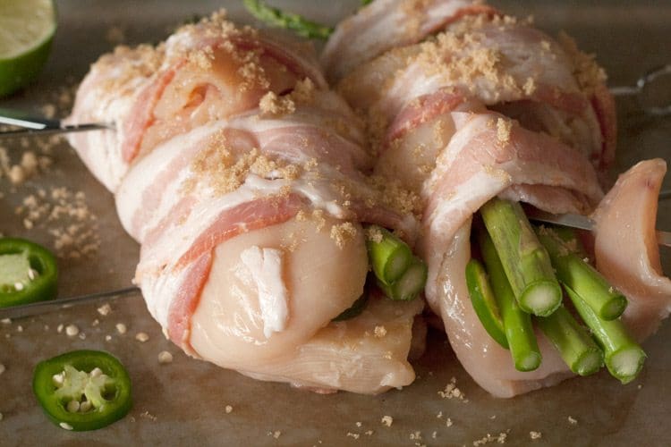 Close-up of chicken breasts stuffed with asparagus and jalapeño slices, wrapped in bacon and sprinkled with brown sugar