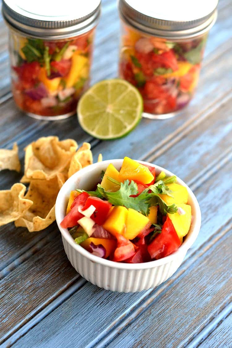 Mango Salsa in a bowl with jars of mango salsa behind it