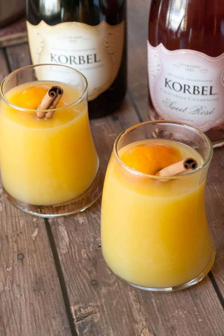 Two glasses of warm mulled mimosa cocktail with cinnamon sticks on a wooden table