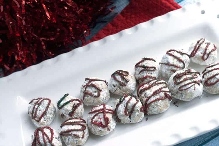 Peppermint snowball cookies with chocolate drizzle and red and green sprinkles on a white platter