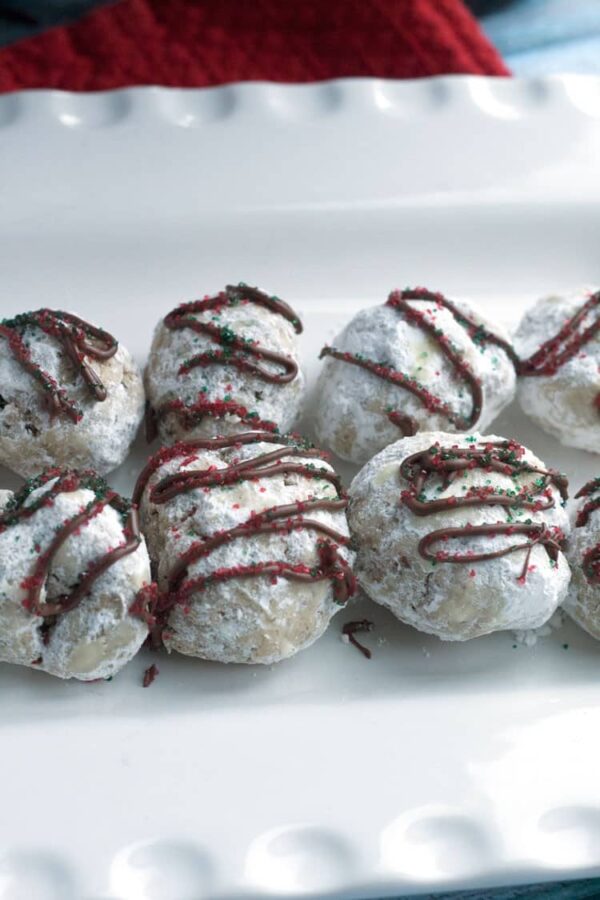 Close-up of peppermint snowball cookies dusted in powdered sugar with a chocolate drizzle