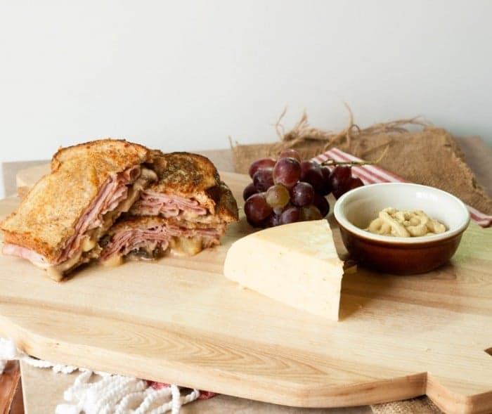 gouda grilled cheese on a serving platter next to gouda, grapes, and mustard in a small bowl