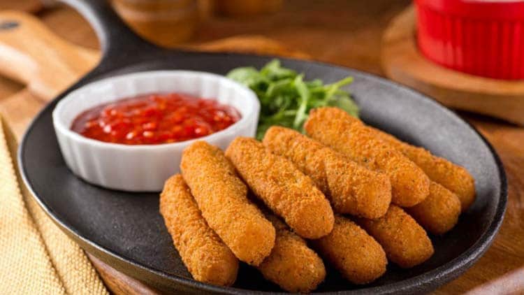 fried mozzarella sticks on cast iron pan with sauce in white bowl 