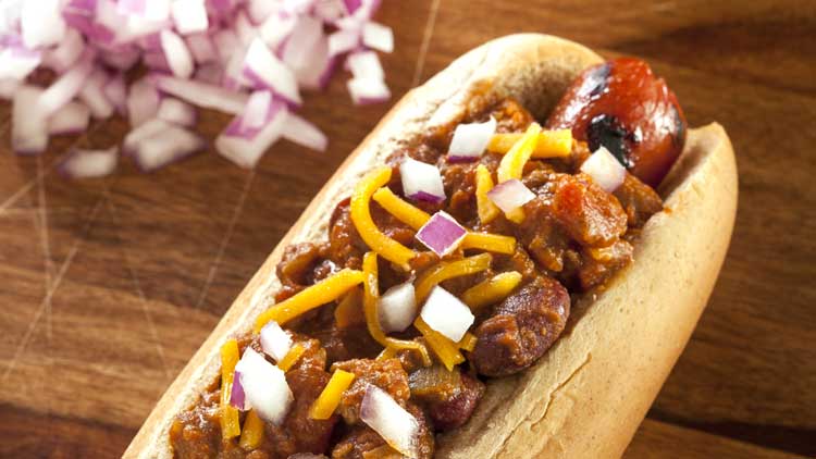 chili dog with onions on wood cutting board