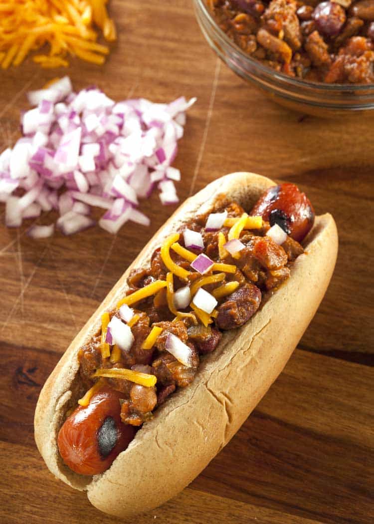 chili dog with onions on wood cutting board