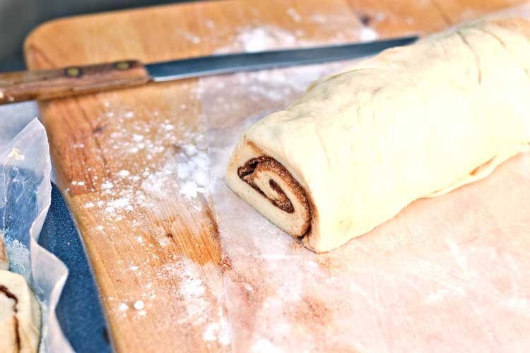 cinnamon roll dough on cutting board to be cut