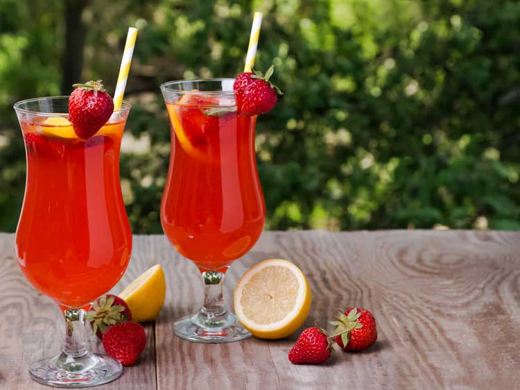 2 hurricane glasses of red drink on wood table outside