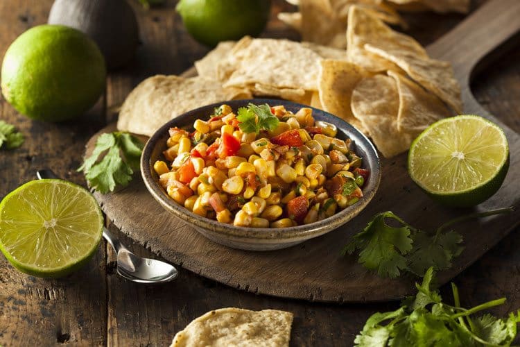 corn salsa and lime halves on rustic wood cutting board