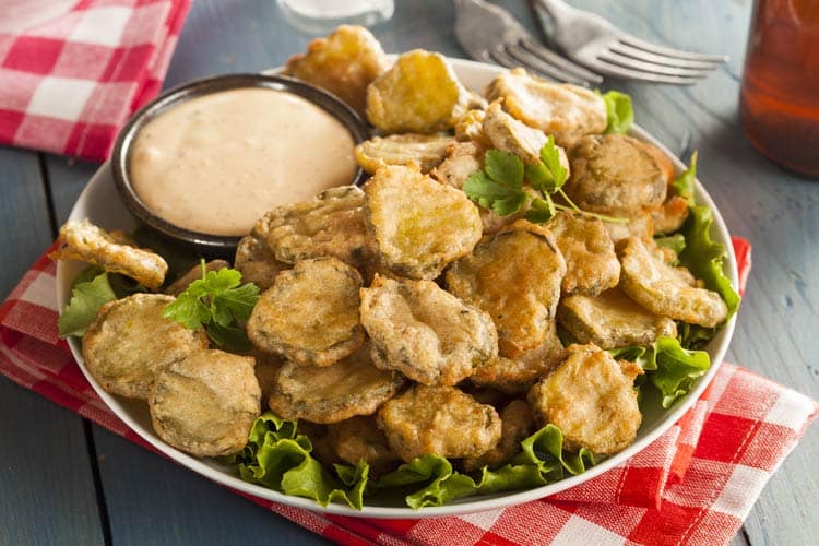 friend pickles on bed of lettuce with dip on the side on white plate