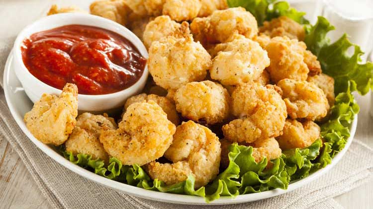 popcorn shrimp on bed of lettuce with cocktail sauce on white plate