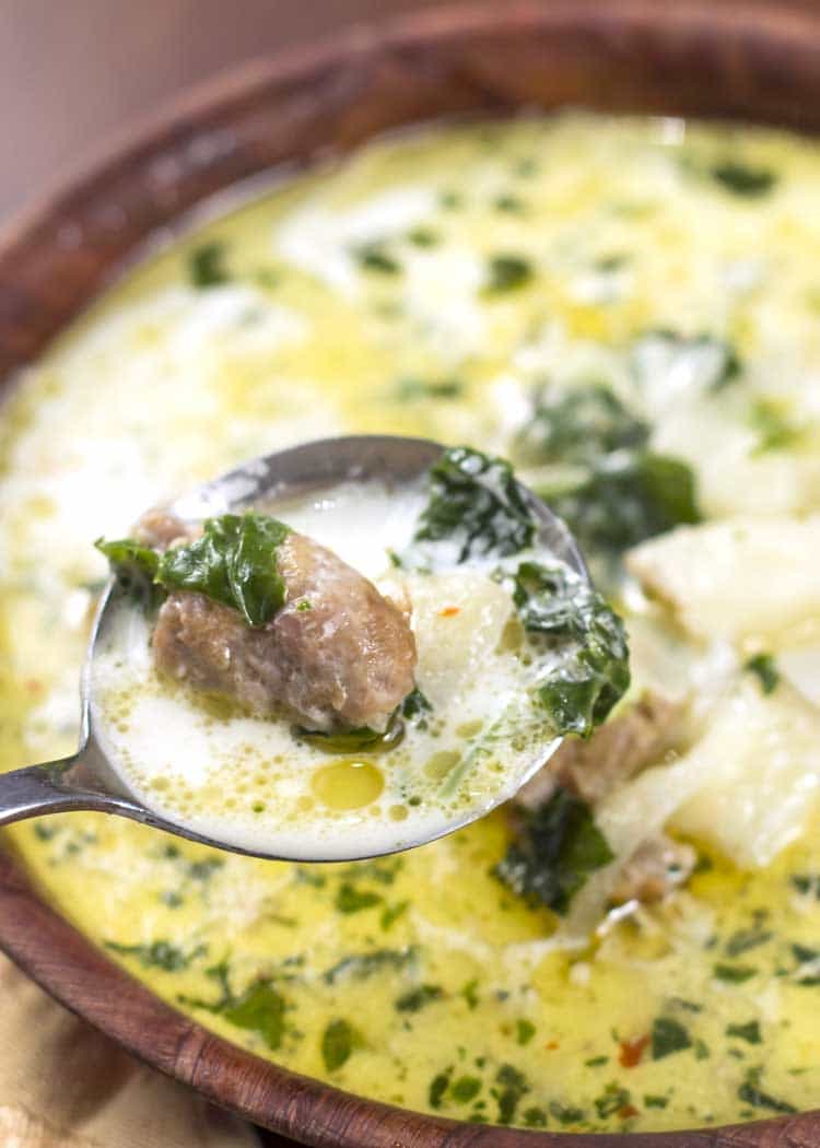 white soup with sausage and kale in brown bowl