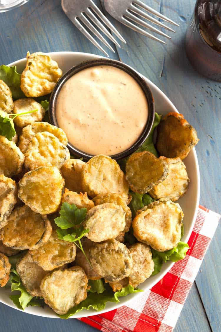 fried pickles with dip on white plate on blue table