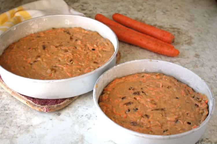 two baking pans containing best carrot cake recipe batter in front of raw carrots