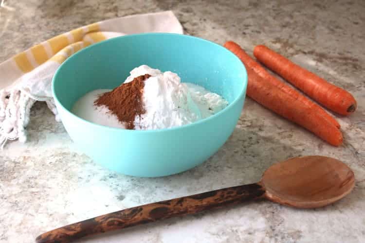 blue bowl containing dry ingredients for best carrot cake recipe next to whole carrots