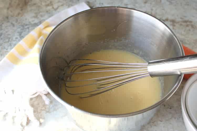 best carrot cake recipe being made with a whisk in the batter in a stainless steel bowl