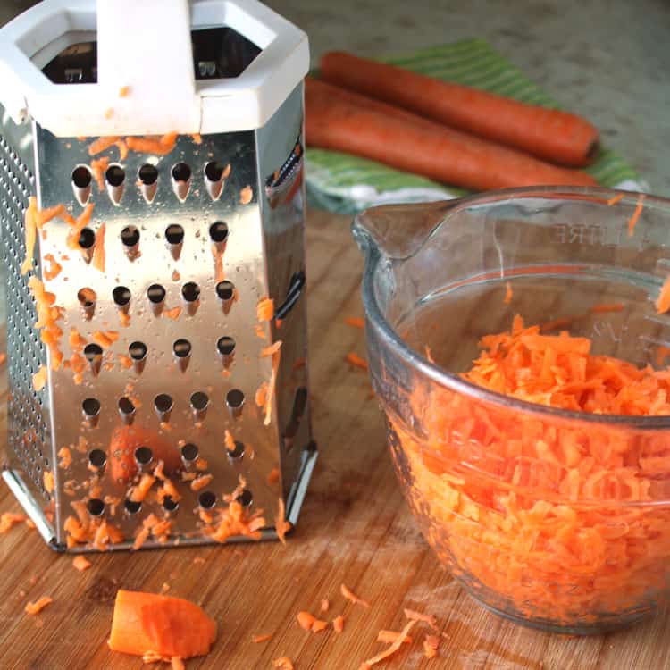 best carrot cake recipe carrots being grated with grated carrots in a clear glass bowl