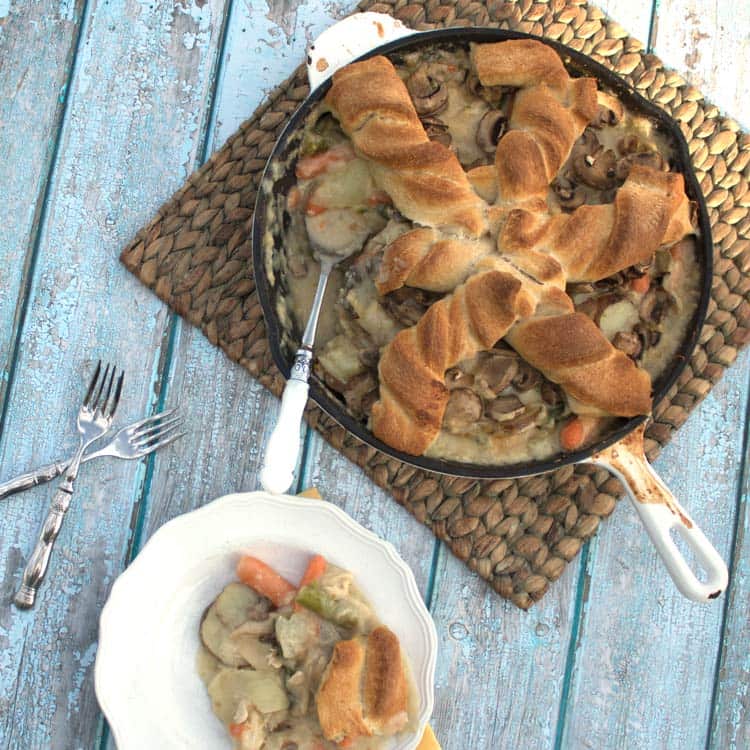 crowd-pleasing chicken pot pie in a skillet next to a plate with a piece on it