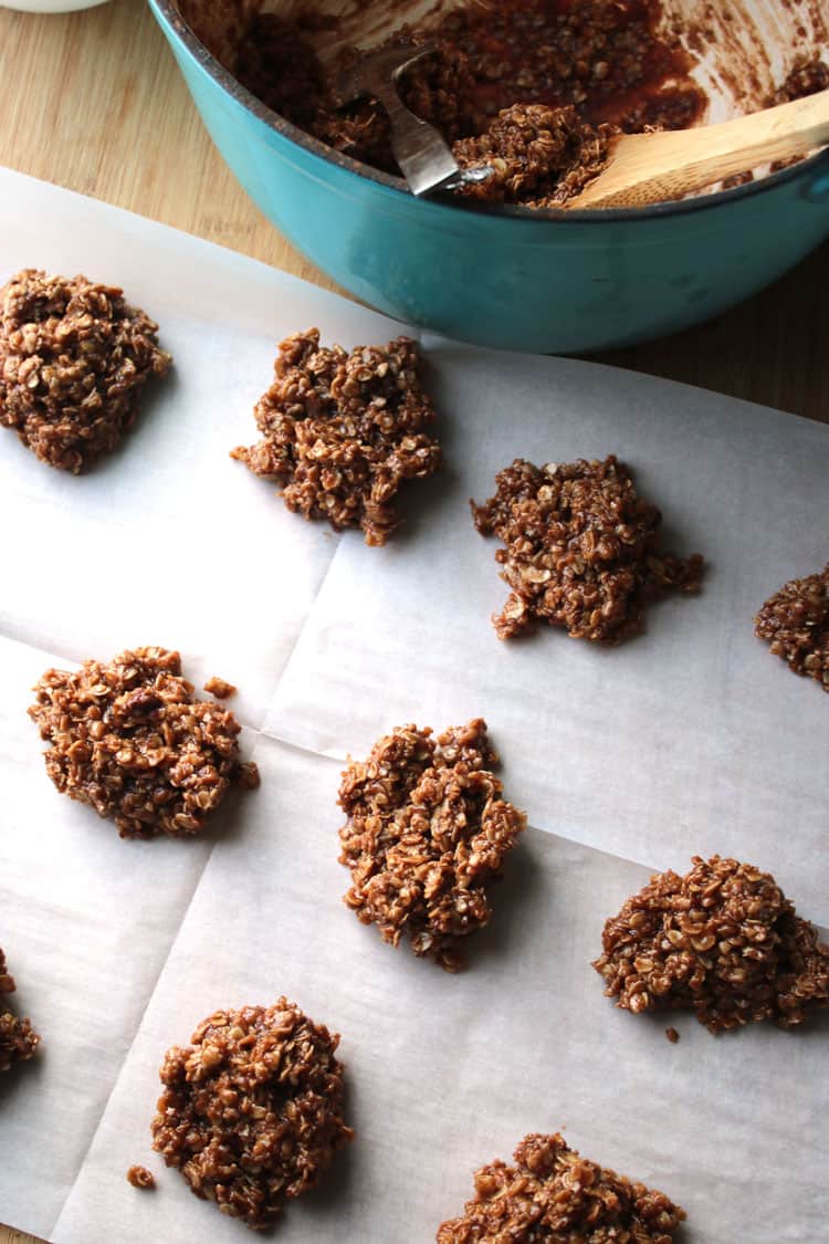 overhead view of no bake chocolate oatmeal cookies on parchment paper next to a blue bowl of batter