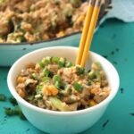 view of white bowl on green counter containing chicken fried rice with chopsticks