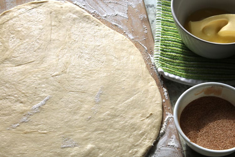 dough for homemade cinnamon rolls rolled out next to container of butter and cinnamon