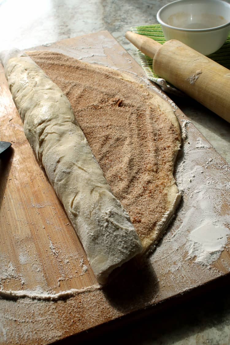 homemade cinnamon rolls dough covered with cinnamon and sugar next to a rolling pin