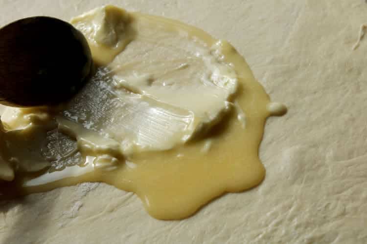 melted butter being spread on top of homemade cinnamon rolls dough