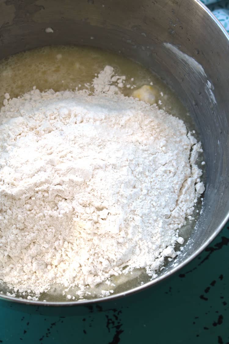 flour poured on top of easy yeast rolls mixture inside stainless steel bowl