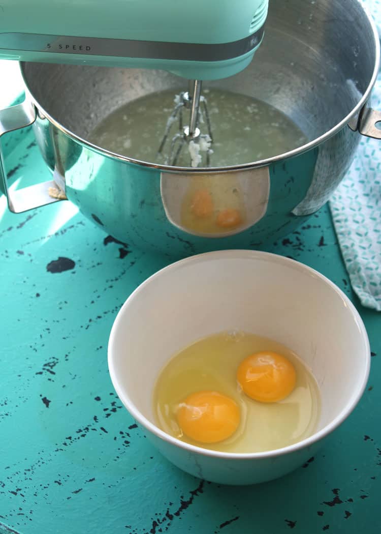 blue mixer in background with mixing whisk inside bowl with white bowl containing eggs in foreground for easy yeast rolls