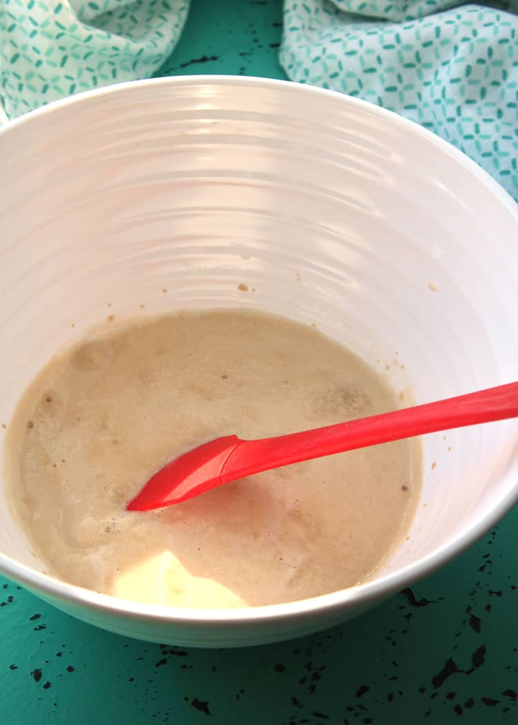 white bowl on top of blue towel containing yeast and water mixture with red spatula for easy yeast rolls