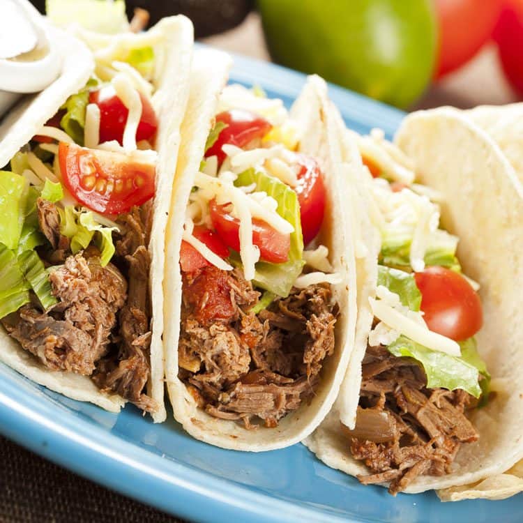 three beef shredded tacos on blue plate