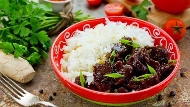 Mongolian rice with beef in red bowl with tomato and cilantro in background