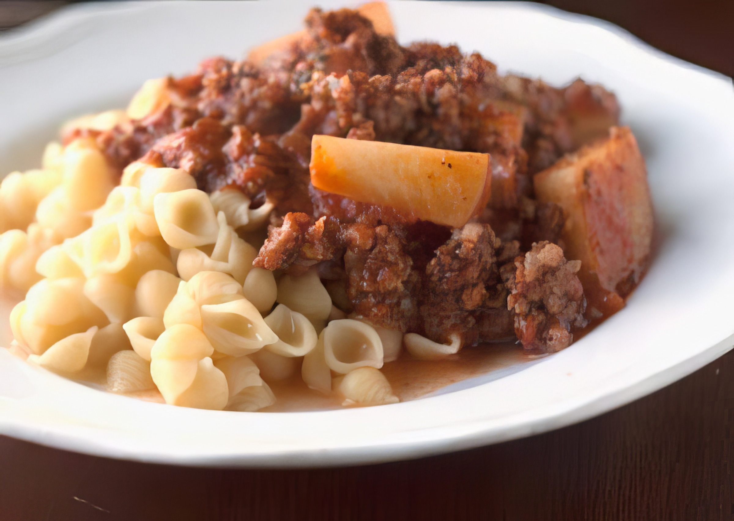 goulash being served with pasta on a white plate