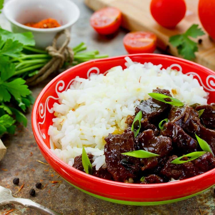 Mongolian rice with beef in red bowl with tomato and cilantro in background