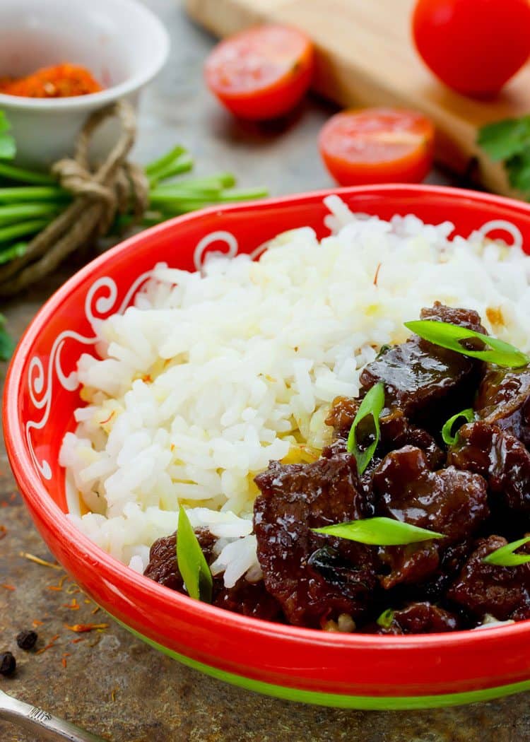 Mongolian rice with beef in red bowl with tomato and cilantro in background