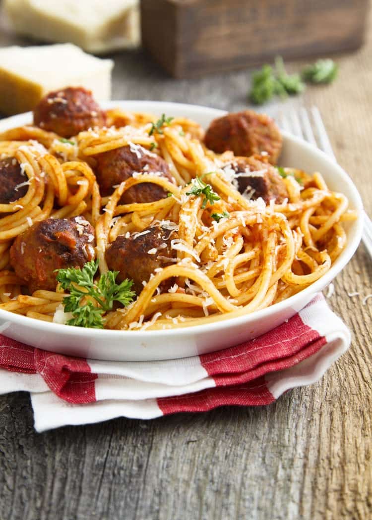 spaghetti with meatballs in white bowl on red and white napkin