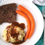 overhead view of cube steak recipes with cube steak, two carrots, and mashed potatoes on a white plate